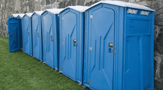 Row of blue portable toilets lined up on grass against a stone wall for event sanitation in Fort Worth, TX