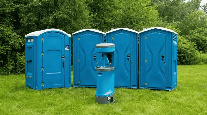 Four blue portable toilets and a matching hand washing station on grass near trees, a common sight at local outdoor events in Fort Worth, TX